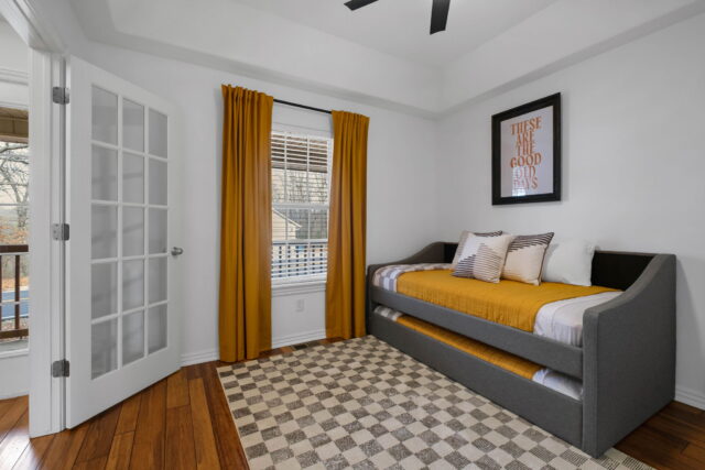 Cozy bedroom with gray daybed, mustard yellow accents, and natural light at The Witherby Woodland Re.