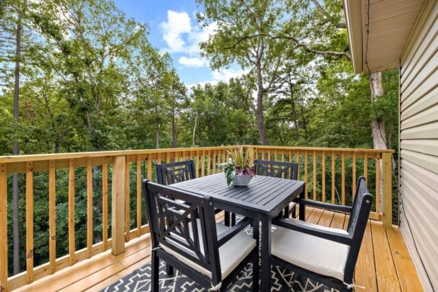 Cozy outdoor balcony with wooden railing and seating, surrounded by lush green trees.