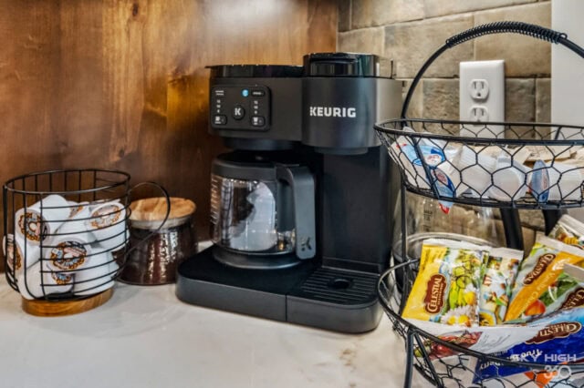 Keurig coffee maker with cups and snacks in a cozy cabin kitchen.