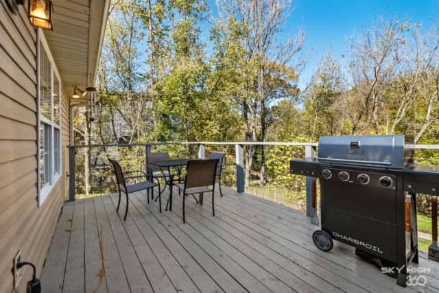 A lush outdoor deck with a grill and seating area overlooking trees and nature.
