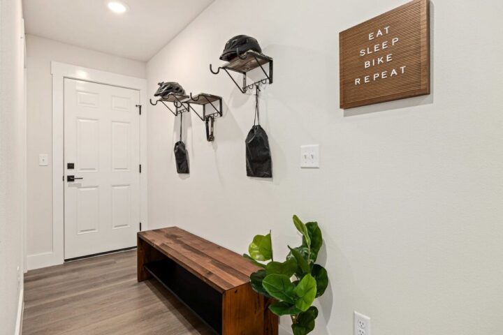 Bike helmets and gear hanging on wall hooks in a modern entryway.