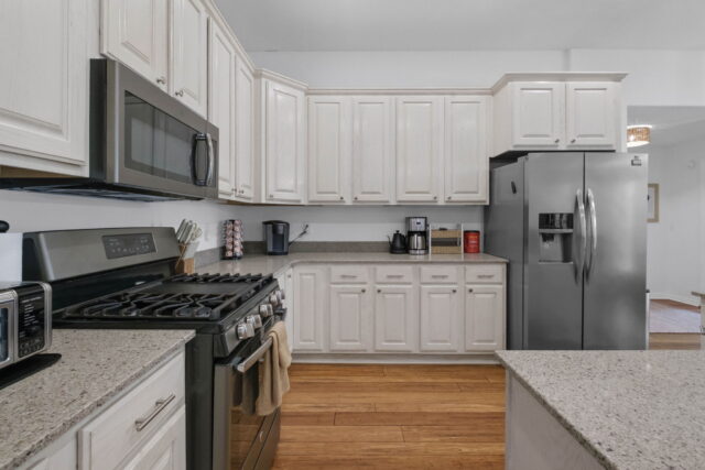 Modern white kitchen with stainless steel appliances and granite countertops at The Witherby Woodlan.