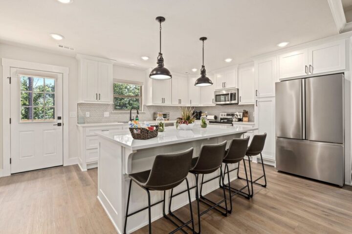 Modern white kitchen with island, stainless steel appliances, and black bar stools near Back 40 Trai.