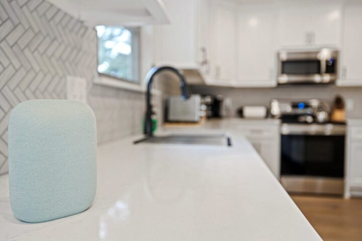 Relaxing smart speaker on a modern kitchen countertop with white cabinets and appliances.