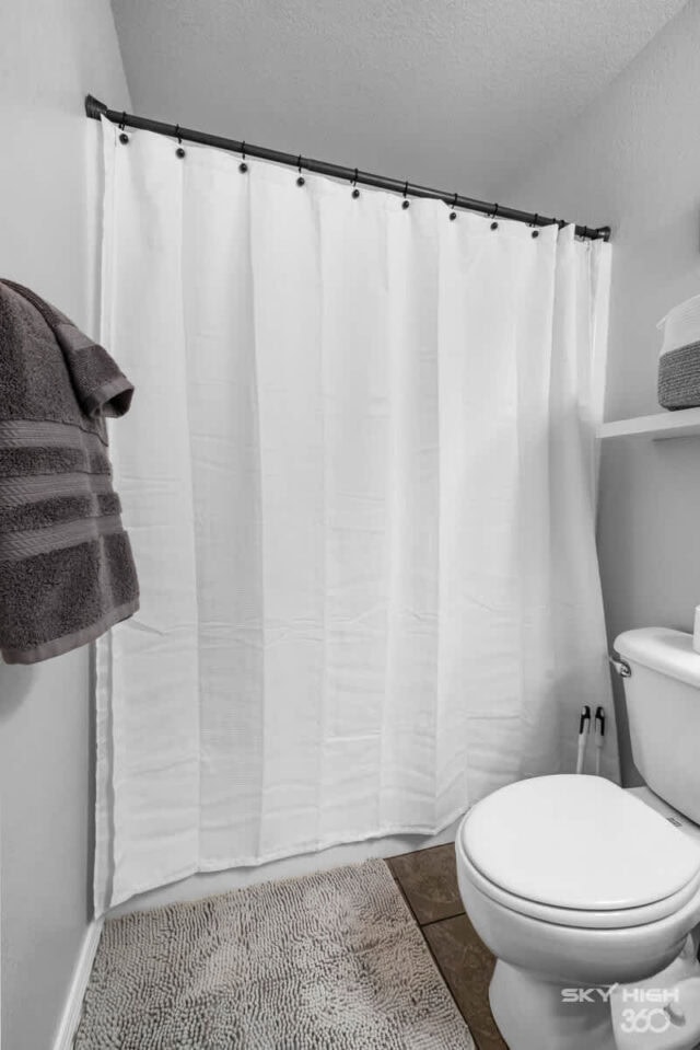 A bathroom with a white shower curtain, toilet, and gray towels in a cozy, clean space near Biker’s.