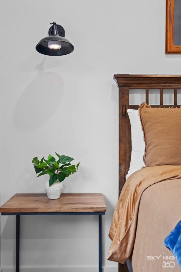 A comfortable bedroom with a wooden bed frame, beige bedding, a side table with a potted plant, and.
