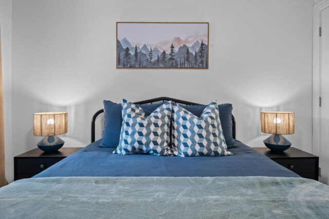 Cozy bedroom with mountain artwork, blue bedding, and modern lamps at The Witherby Woodland Retreat.