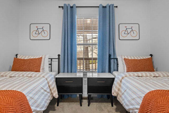 Cozy bedroom with two twin beds, blue curtains, and bicycle artwork, near Back 40 Trails at Bella Vi.