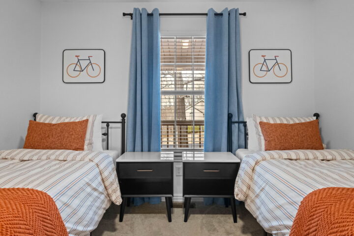 Cozy bedroom with two twin beds, blue curtains, and bicycle artwork, near Back 40 Trails at Bella Vi.
