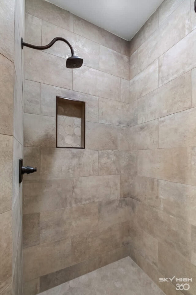 A lush, modern walk-in shower with beige tile walls and a built-in niche for toiletries.