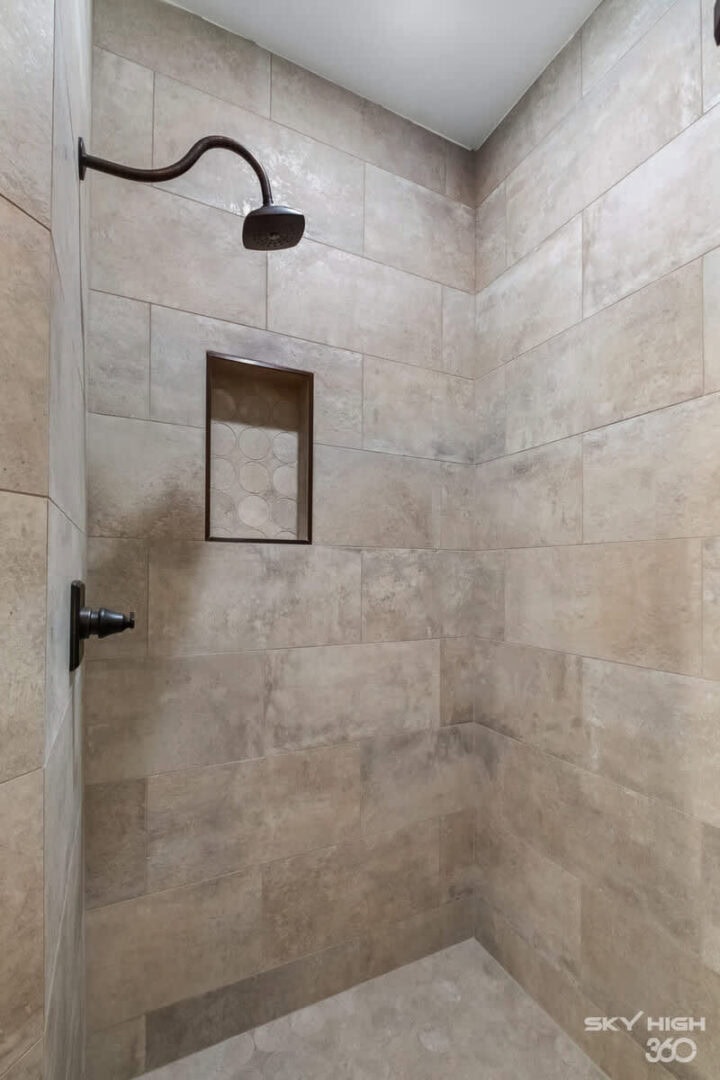A lush, modern walk-in shower with beige tile walls and a built-in niche for toiletries.