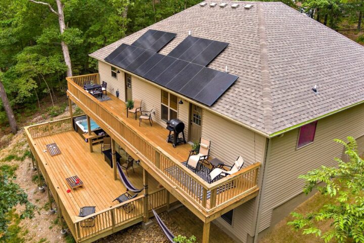 Solar panels installed on the roof of a cozy vacation rental house with a large wooden deck surround.