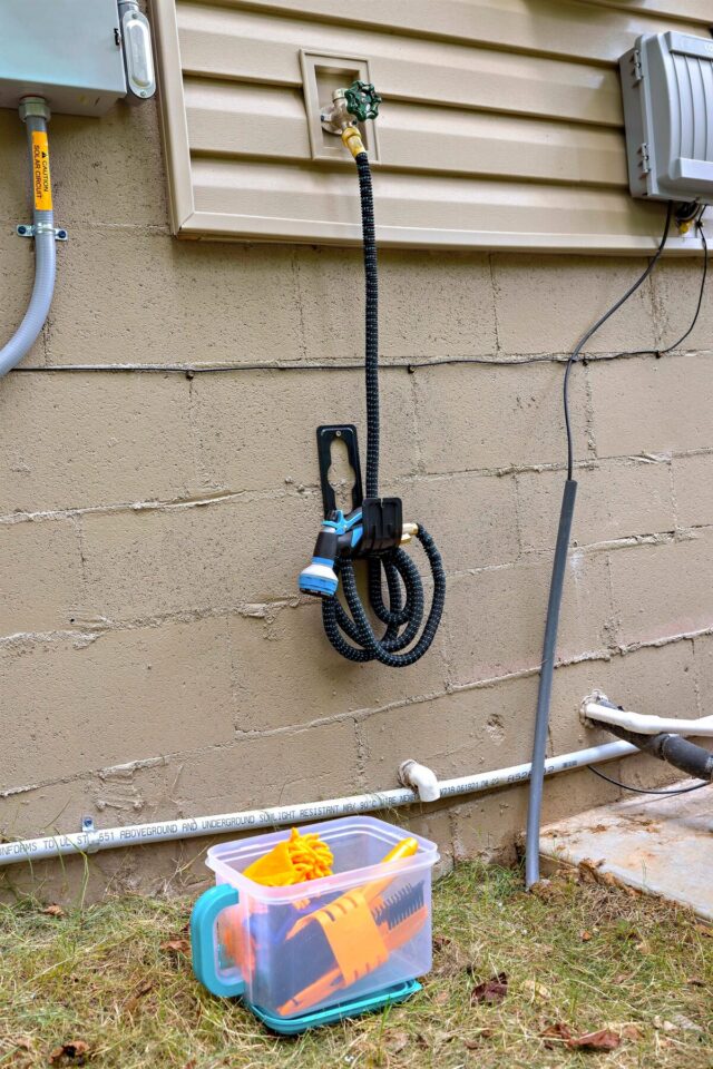 A colorful garden hose and spray nozzle hanging on a beige exterior wall.