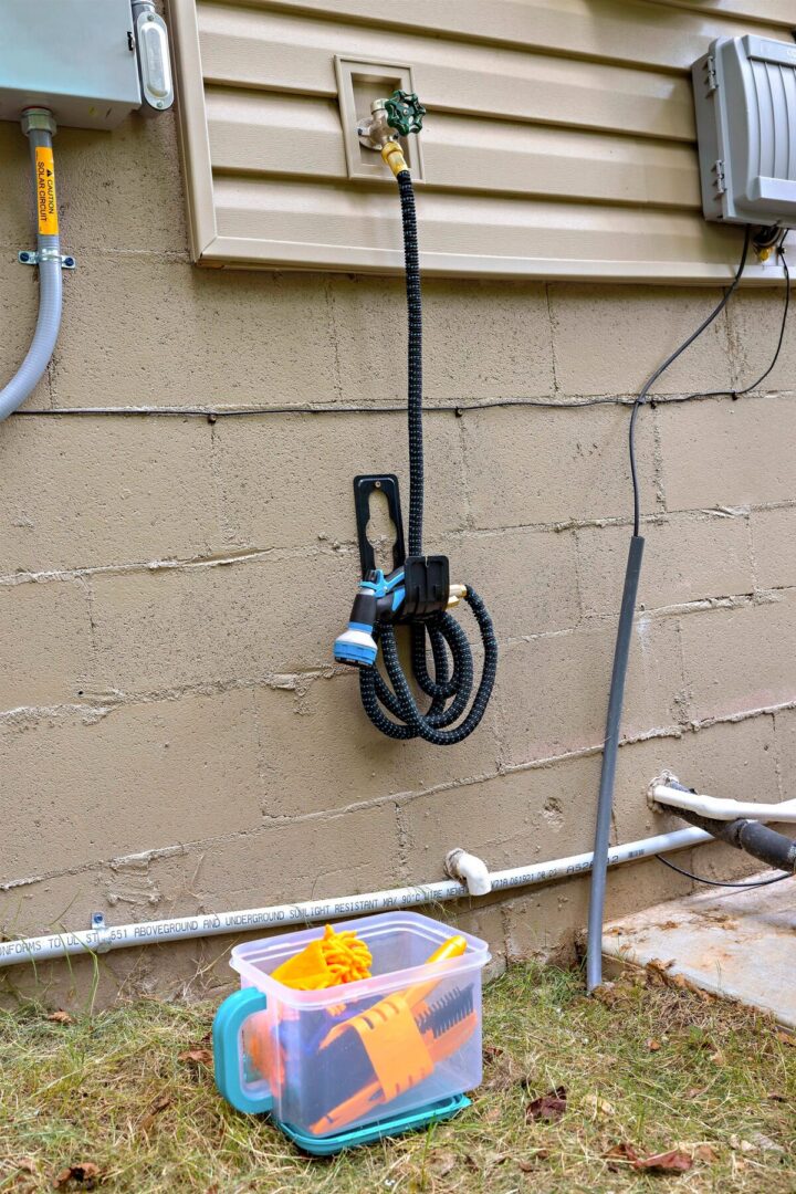 A colorful garden hose and spray nozzle hanging on a beige exterior wall.