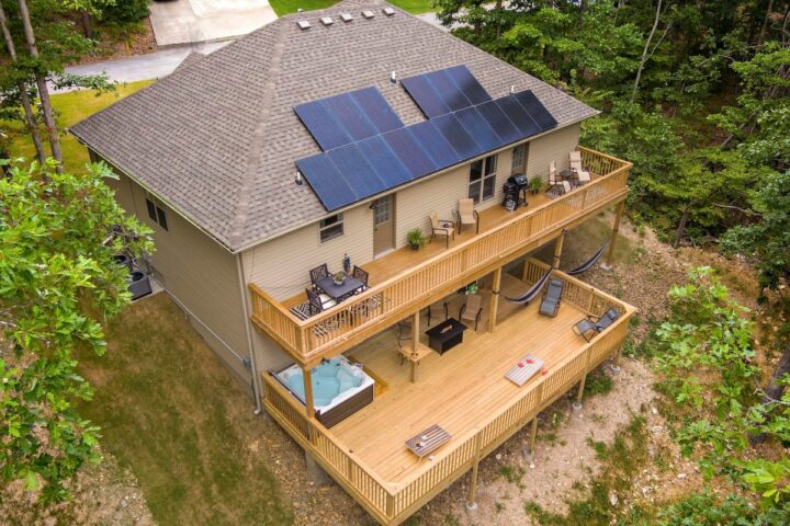 Solar panels on the roof of a modern vacation rental home with large outdoor decks surrounded by tre.