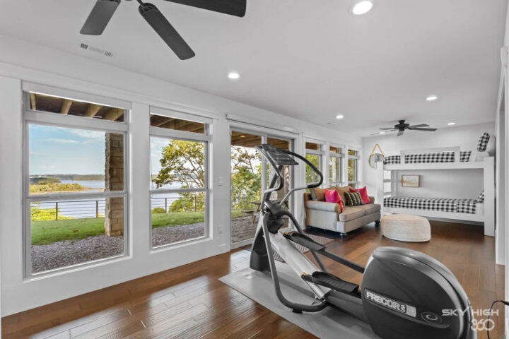 Bright living room with large windows overlooking Beaver Lake, featuring a treadmill and cozy seatin.
