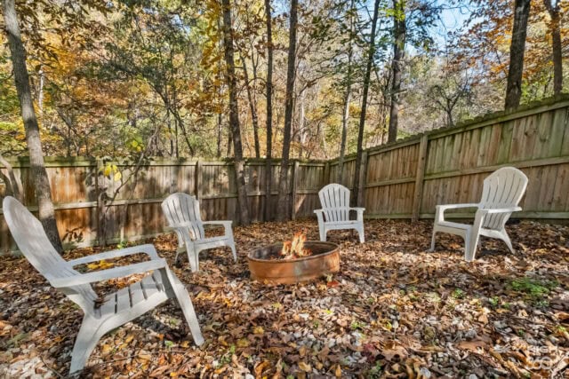 Relaxing outdoor fire pit area with Adirondack chairs in a wooded backyard during fall.