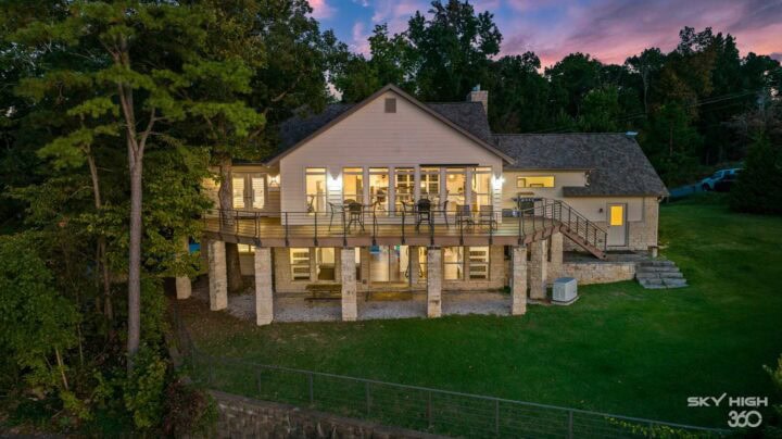 Relaxing river view vacation rental at dusk with illuminated interior in Rogers, AR.
